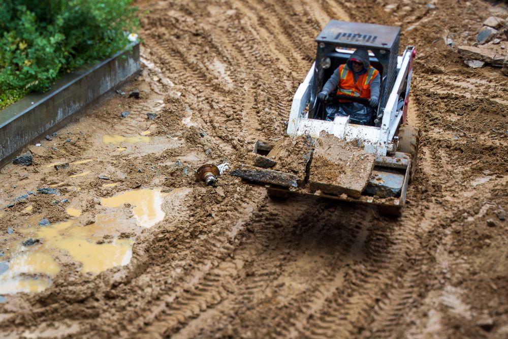 A skid steer moving wet soil beside a planter