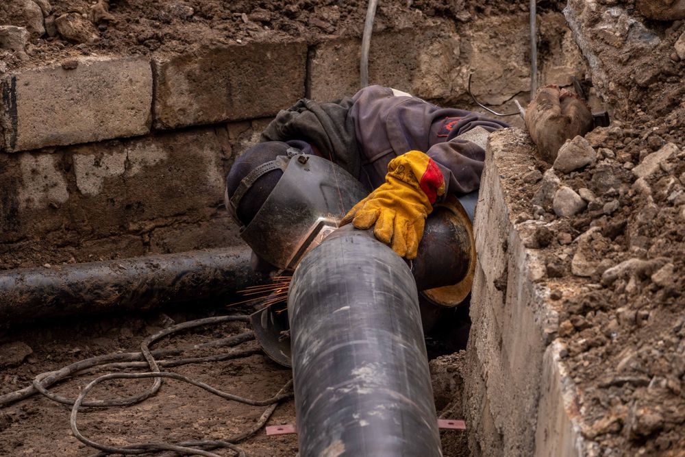 A worker down in a trench working on a pipe